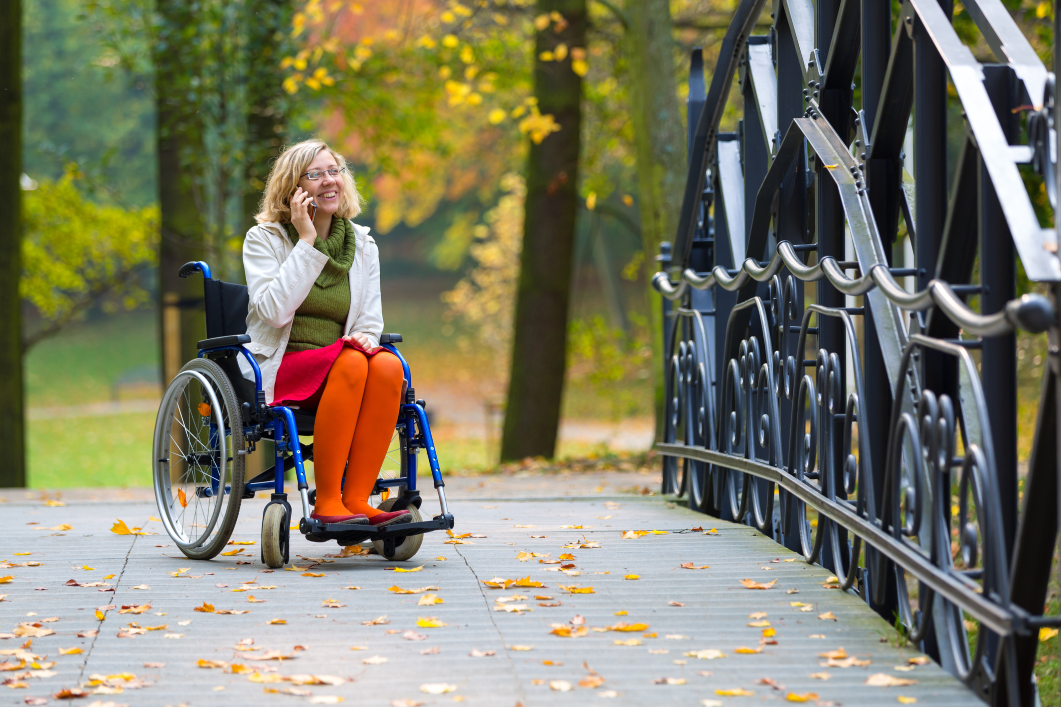 Happy woman on wheelchair talking on the phone in the park in autumn.