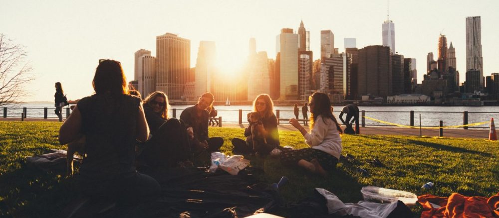 Group of friends having a picnic in a park with New York City skyline behind them