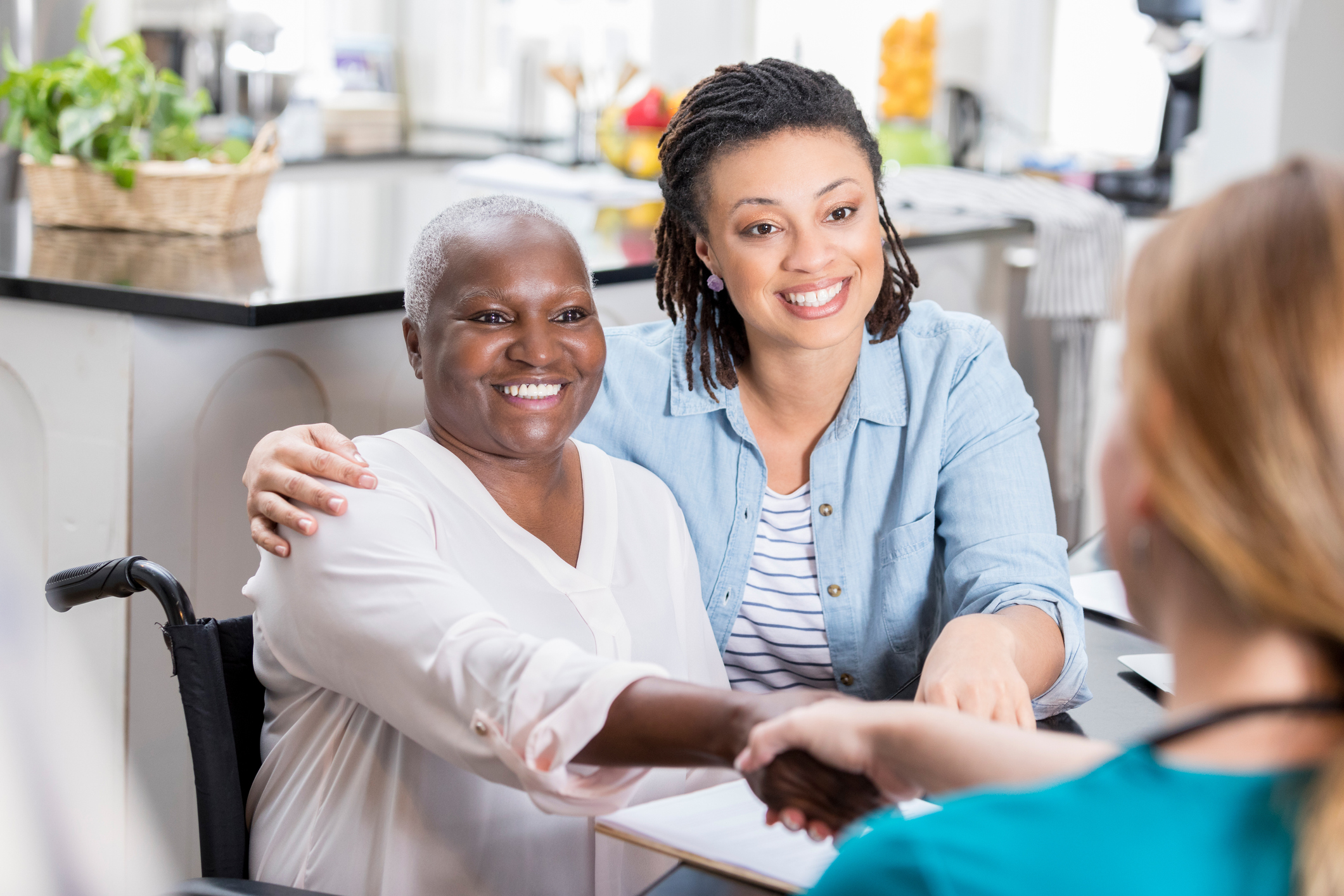 A woman talks with her mom's home healthcare nurse. The daughter has her arm around her mom. The mother is shaking the nurse's hand.