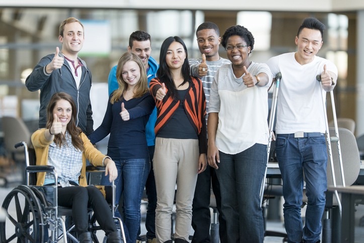 Diverse group of college students smiling and showing a thumbs up. One of them is in wheelchair and one is with crutches.