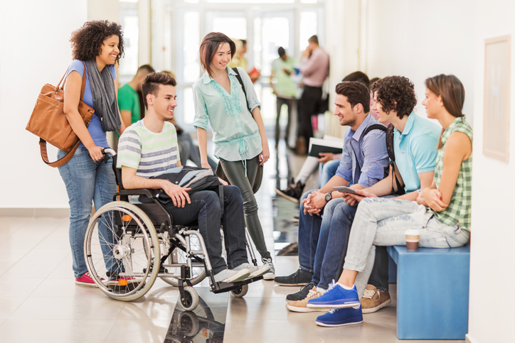 Group of students having a break and talking to each other in the corridor. One of them is in a wheelchair.