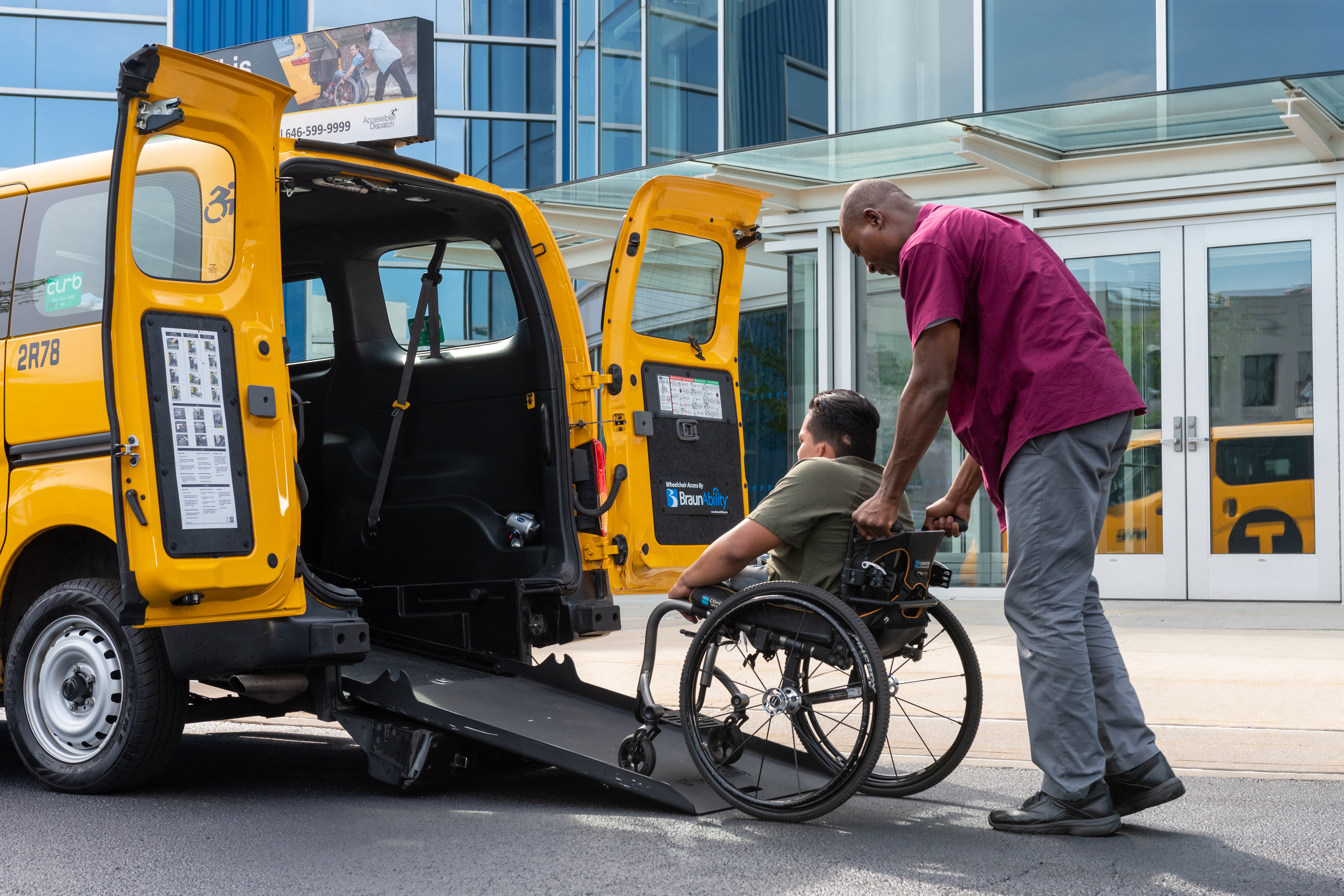 A TLC-Licensed yellow cab driver helping a passenger with wheelchair board a Nissan NV200.