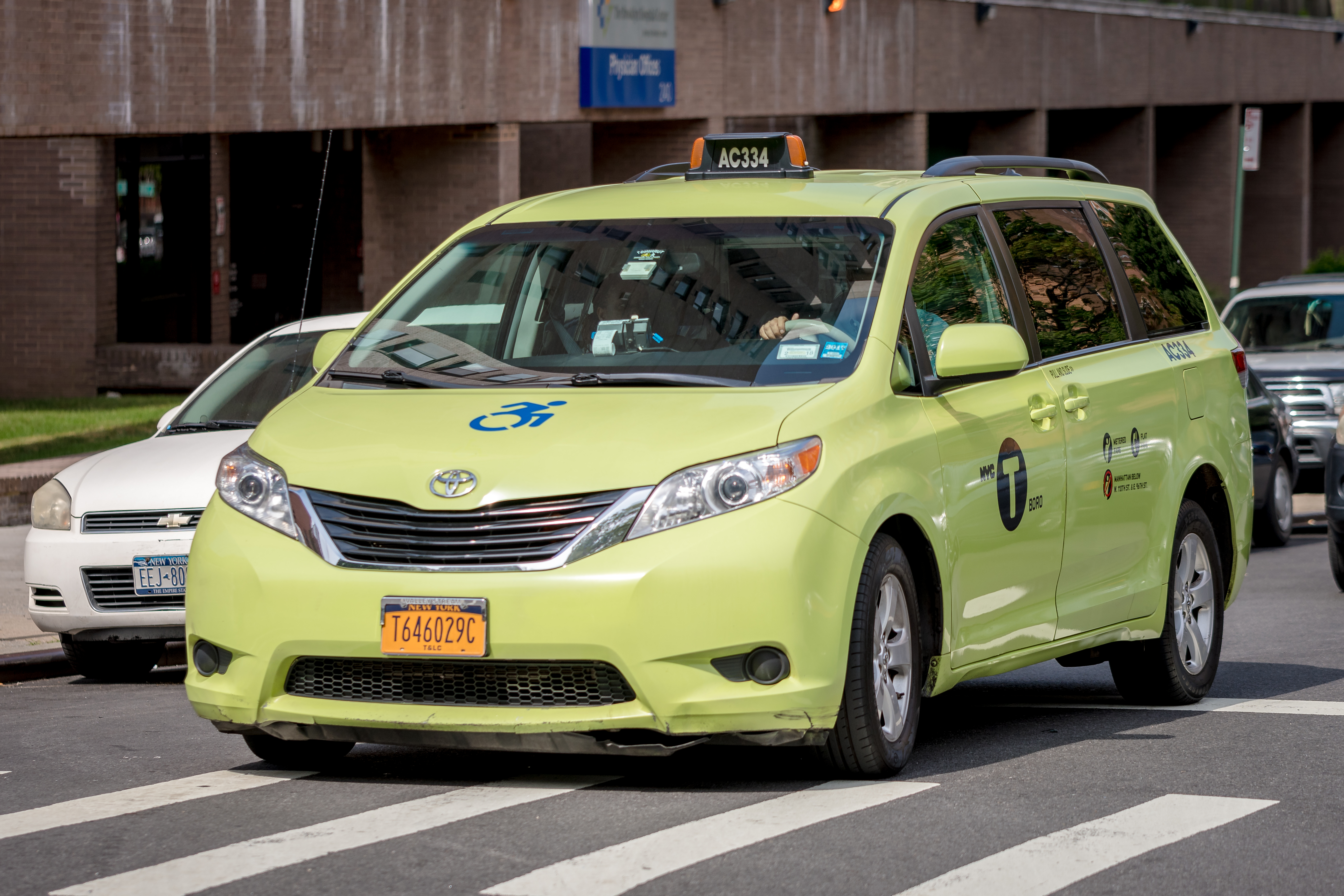 A green wheelchair accessible Toyota Sienna travels down a New York City street.